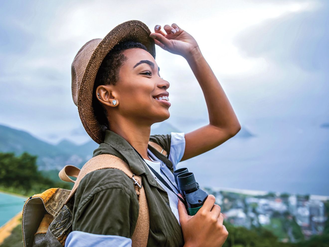 Young woman lifting her hat to get a better view, with a tropical scenery in the background
