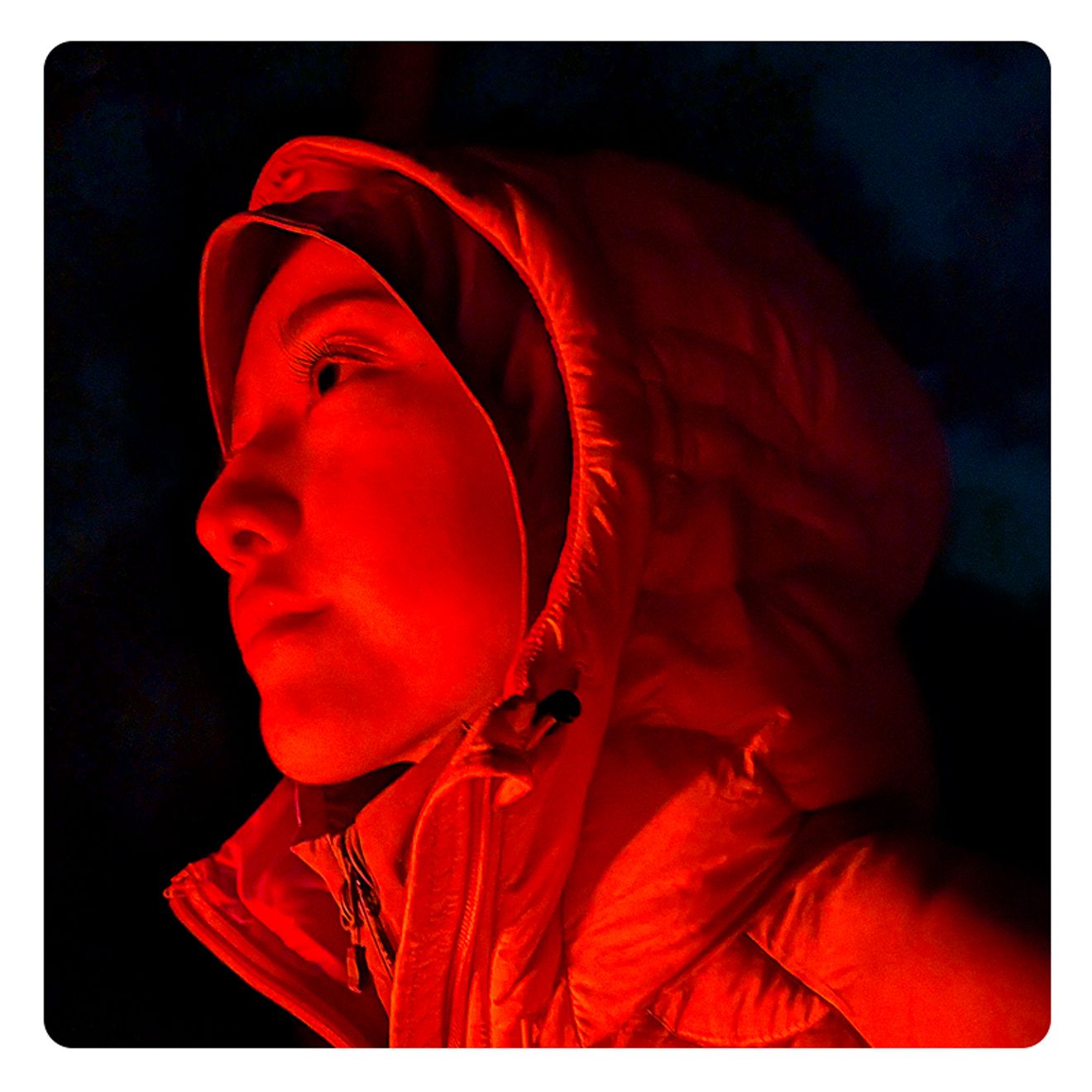 Close-up of a person bundled in a parka, dramatically lit at night