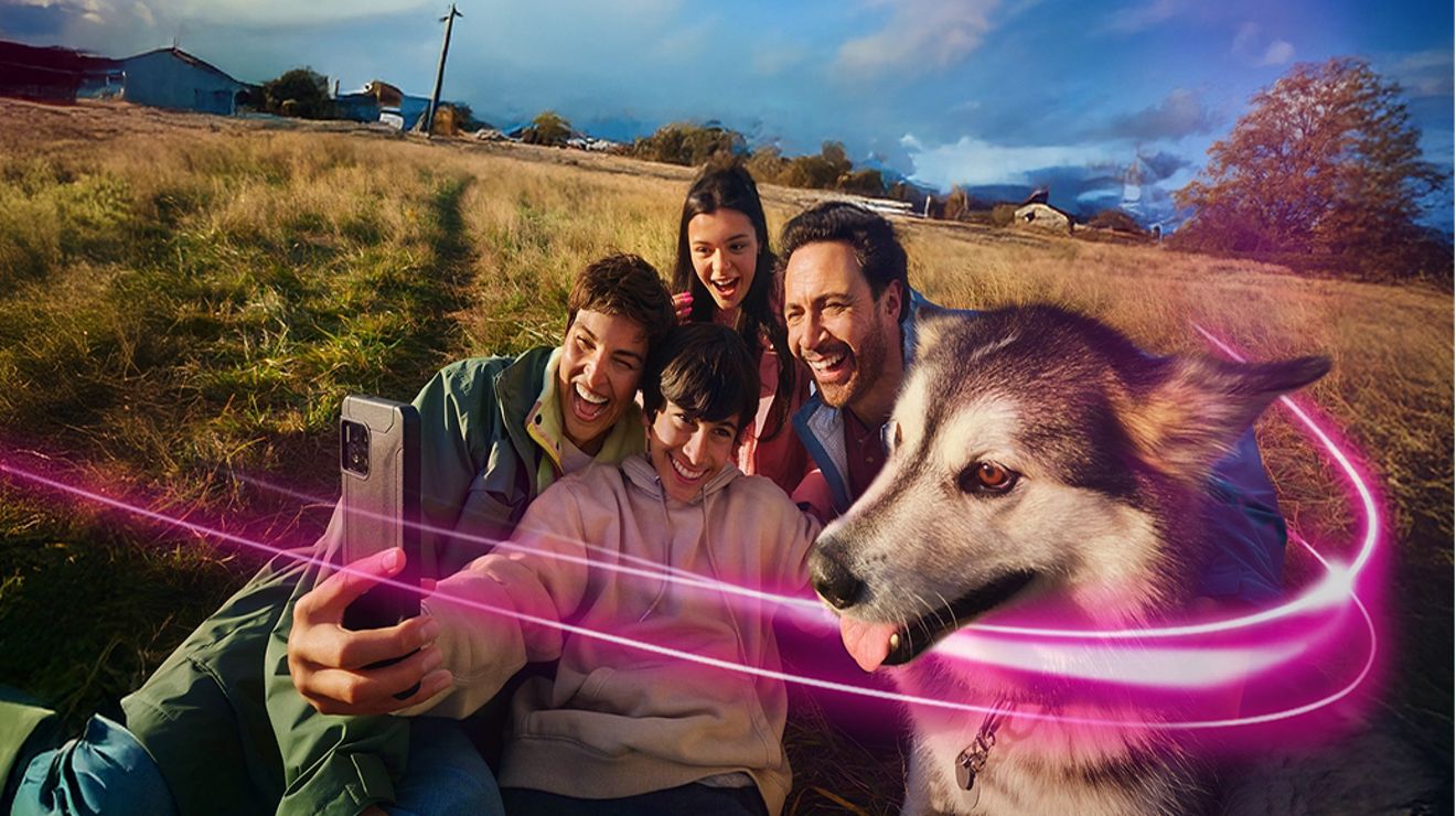 Four people and a husky dog take a selfie outside.