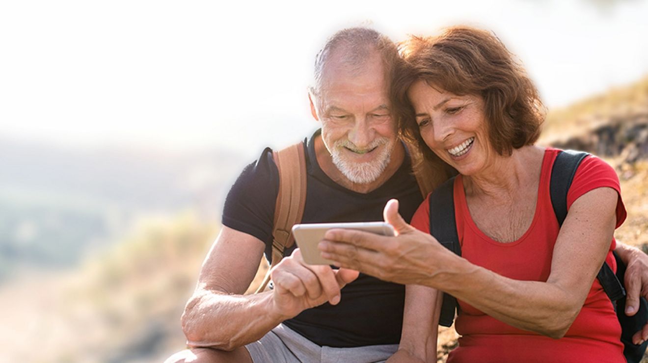 An older couple looks at a phone while on a hike.