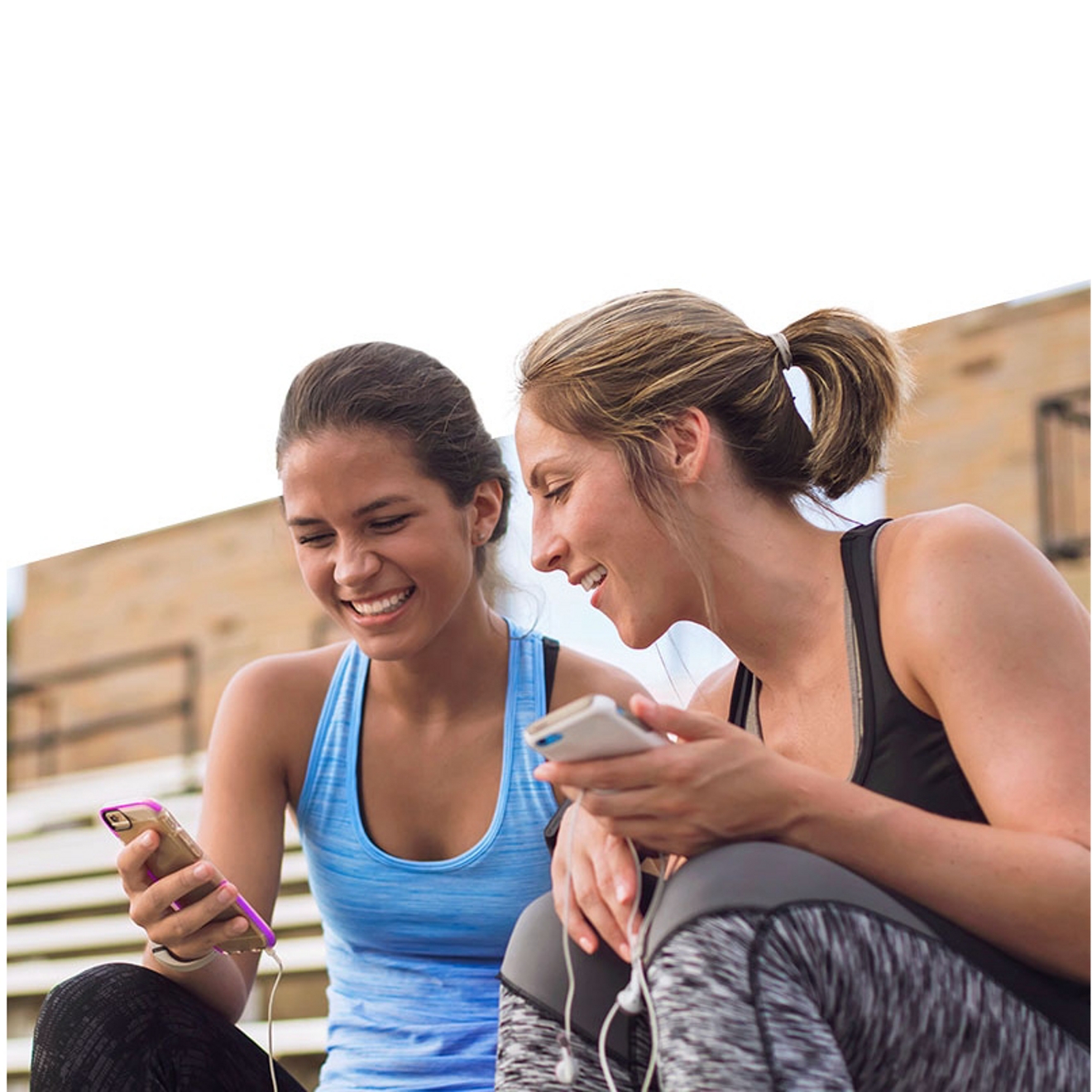 Two friends looking at their phones and smiling.
