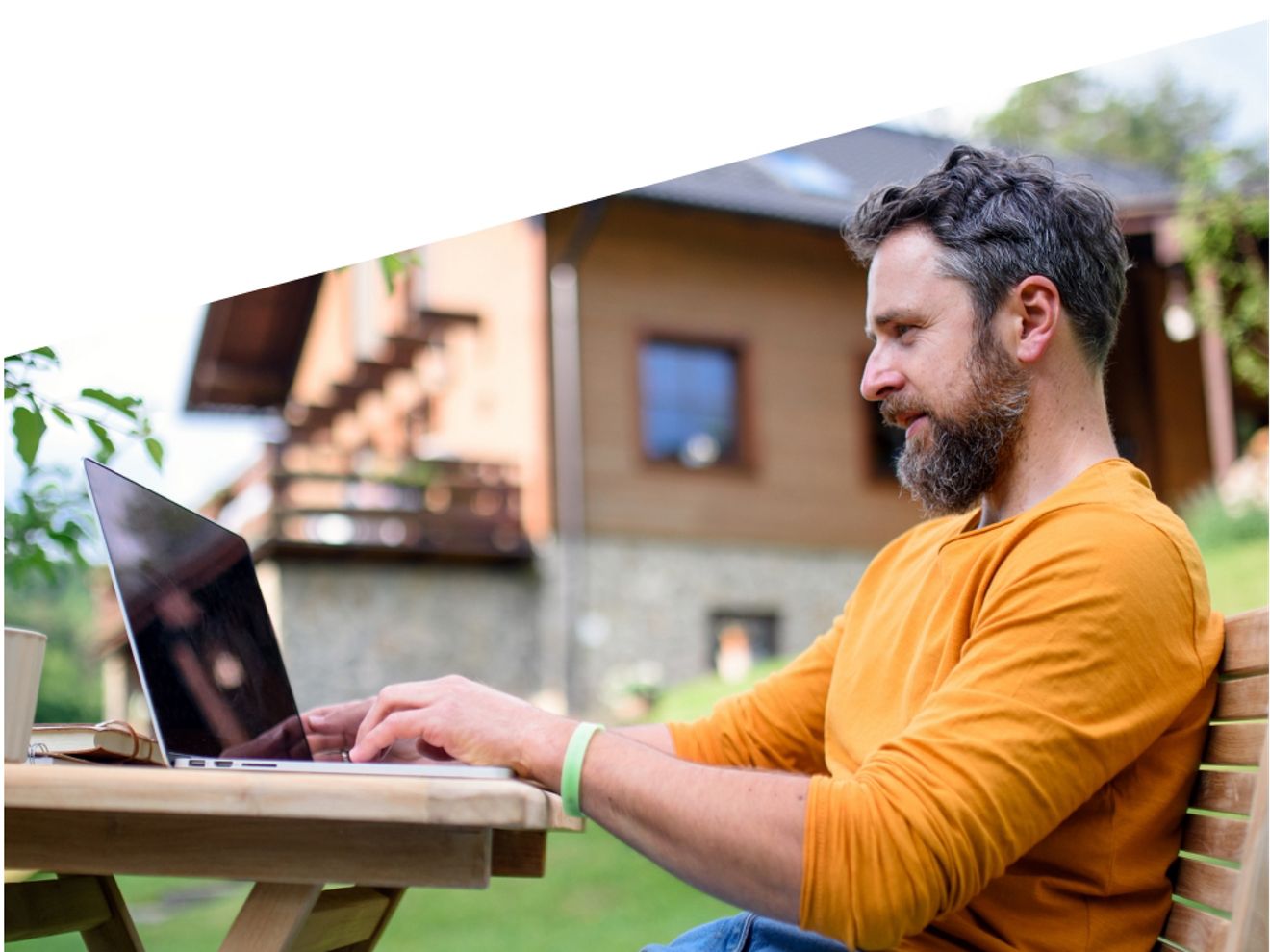 A man works on his laptop at a table in his backyard