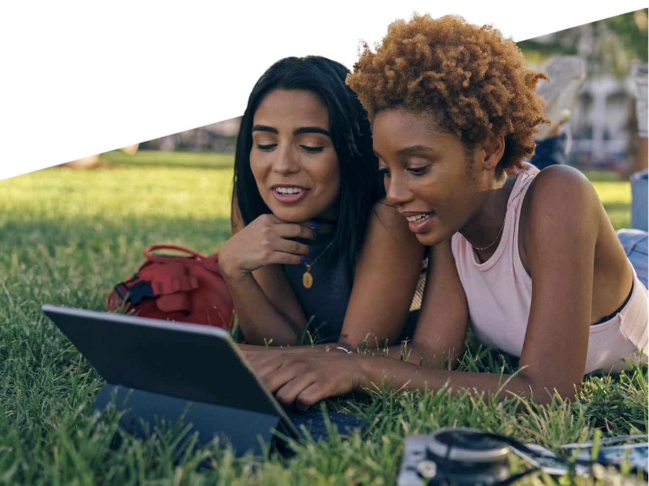 Two women using a tablet on the grass in a park
