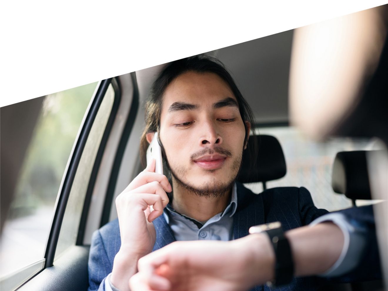 A man in the passenger seat talks on a phone while looking at his smartwatch