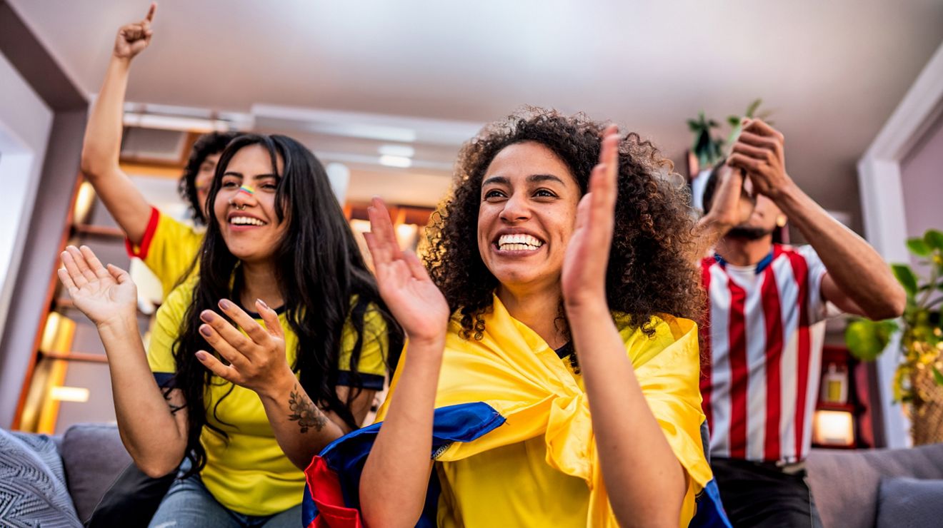 Three friends cheering and clapping while watching a sports game at home.