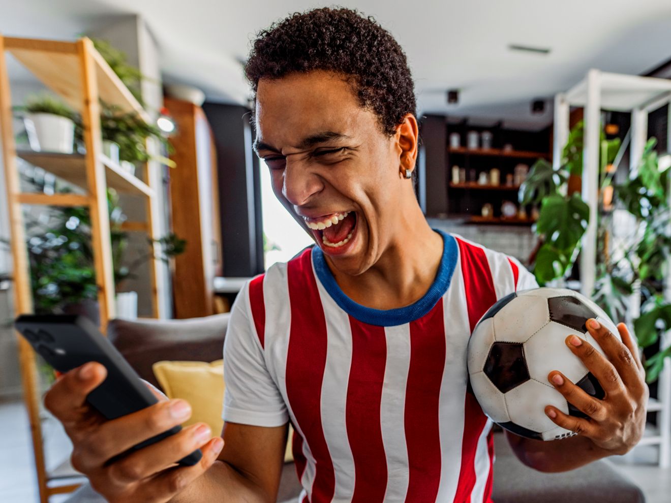 Man standing in his living room laughing while staring at his cellphone.