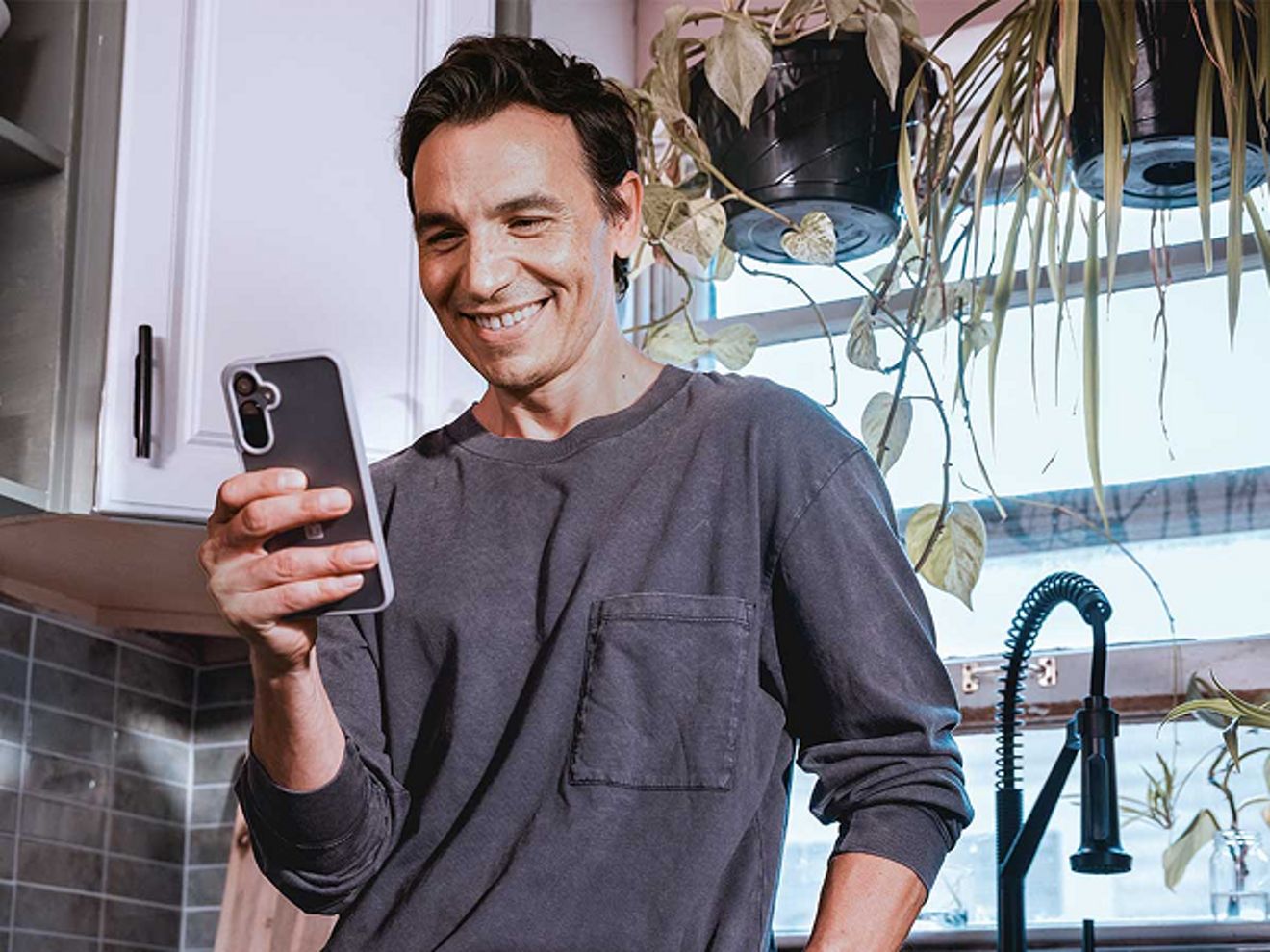 Un hombre mira un video en un smartphone en la cocina.