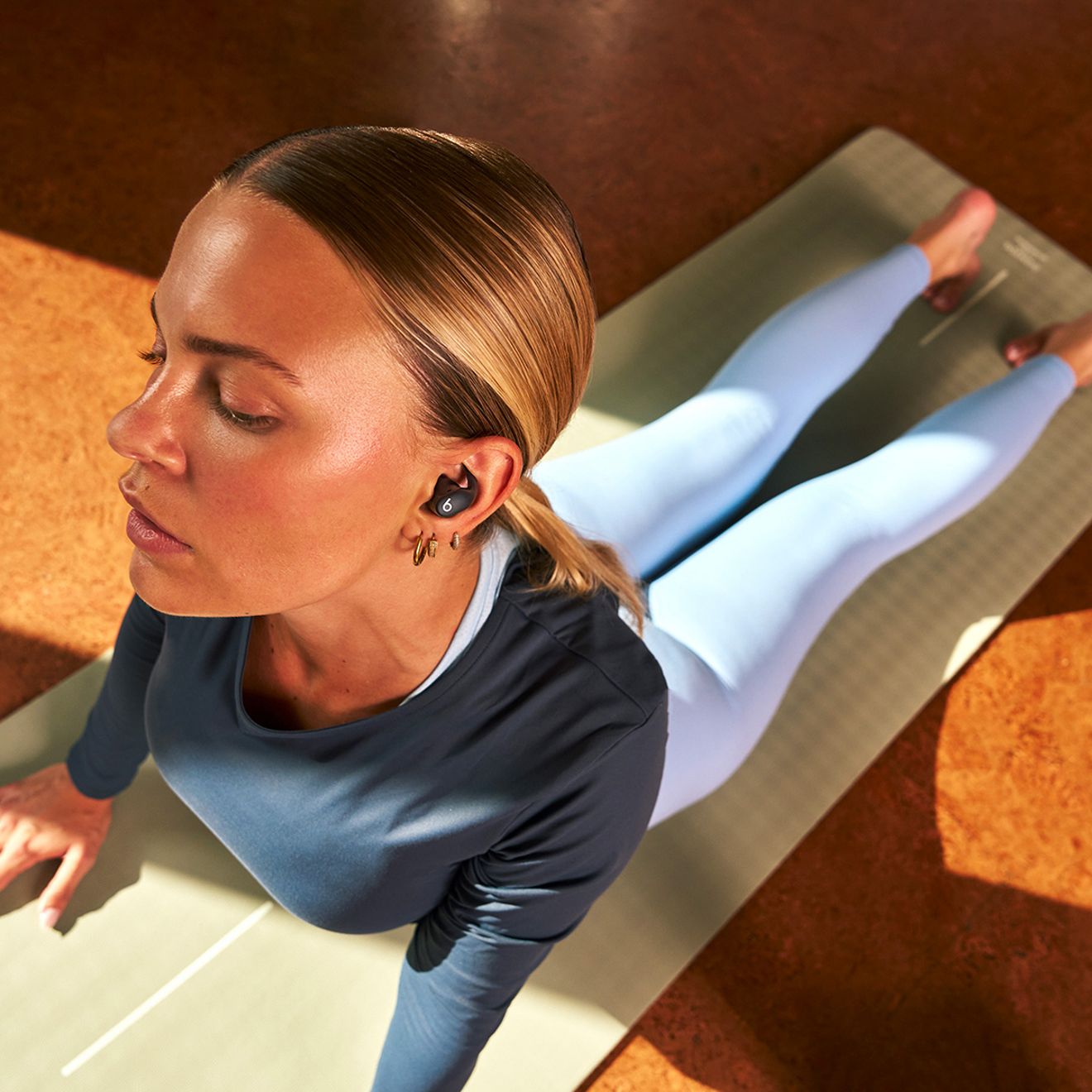 A woman is working out and stretching while wearing her Beats Powerbeats Fit.