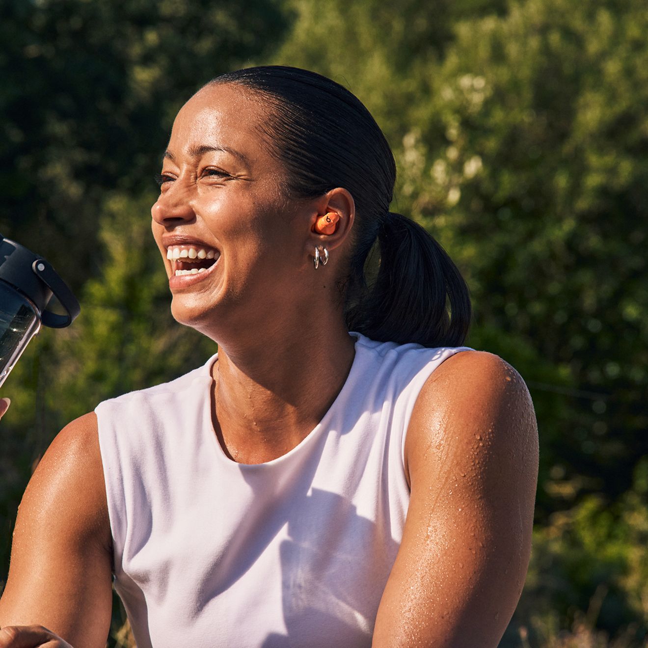 A woman smiles while outside listening to her Beats Powerbeats Fit.
