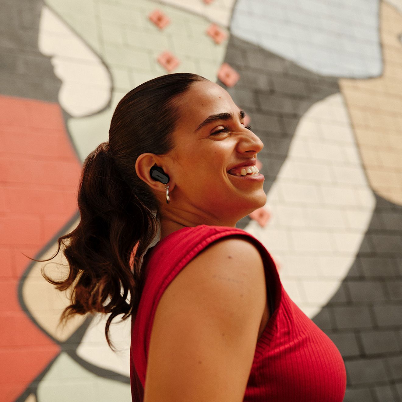 A woman smiles outside while using her Bose Quiet Comfort Ultra Earbuds 2nd generation.