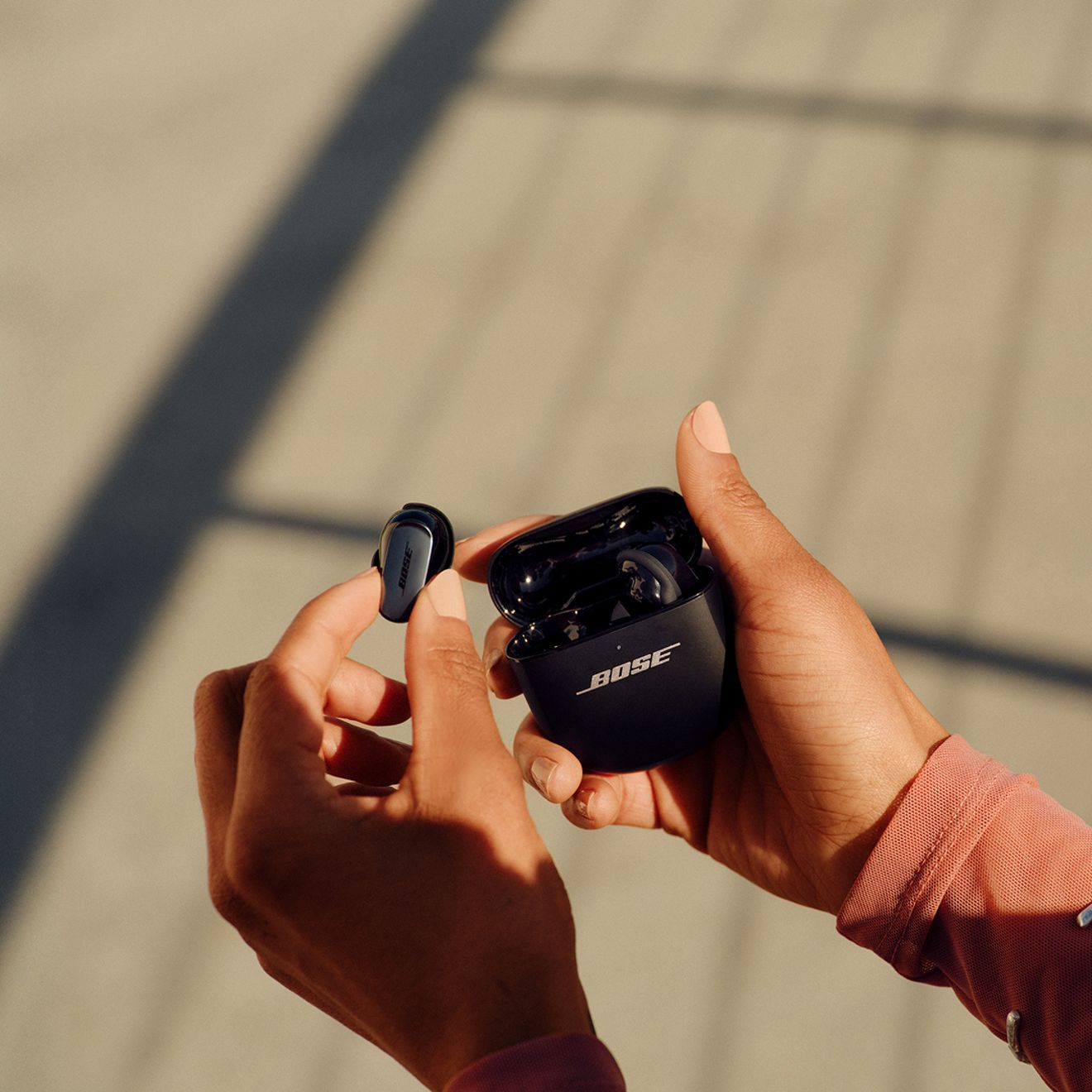 A close-up of two hands holding their Bose Quiet Comfort Ultra Earbuds 2nd generation and the charging case.