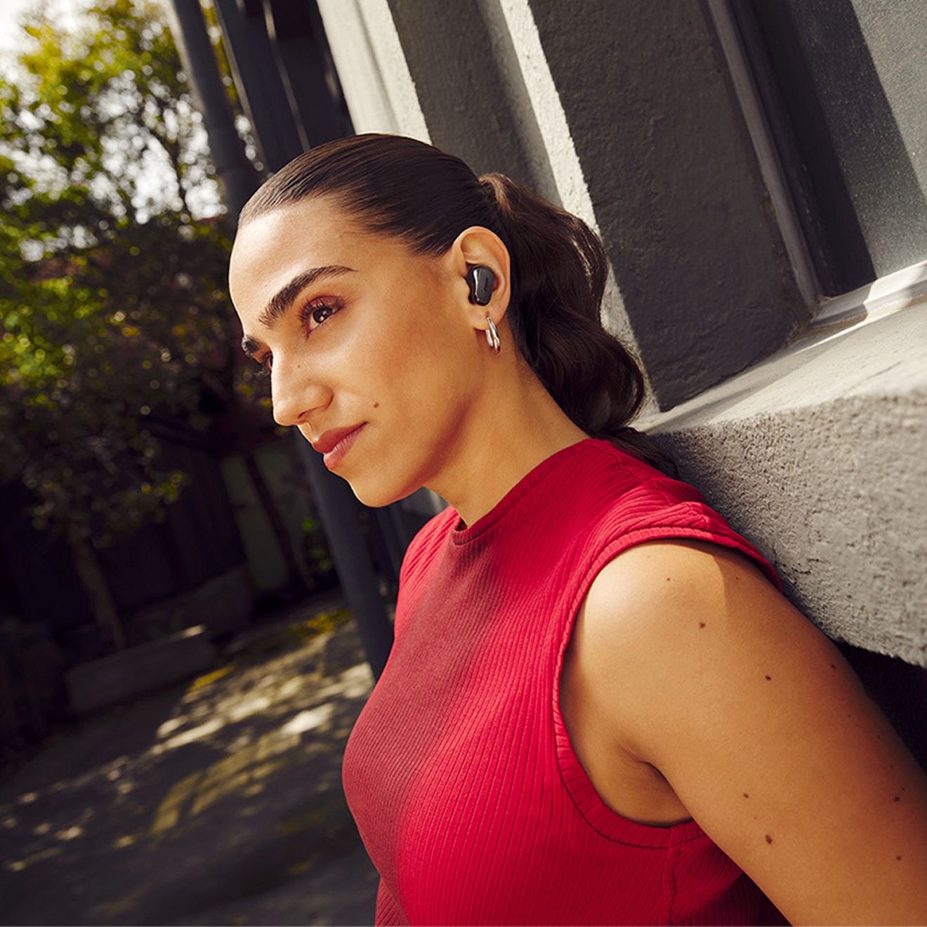 A woman outside leaning up against a wall while listening to her Bose Quiet Comfort Ultra Earbuds 2nd generation.
