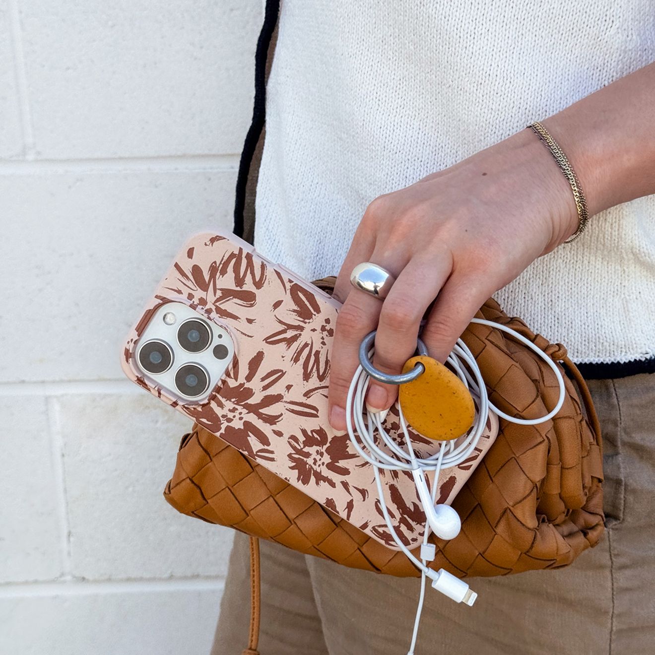 A man holds his iPhone Pela phone case and his iPhone headphones.