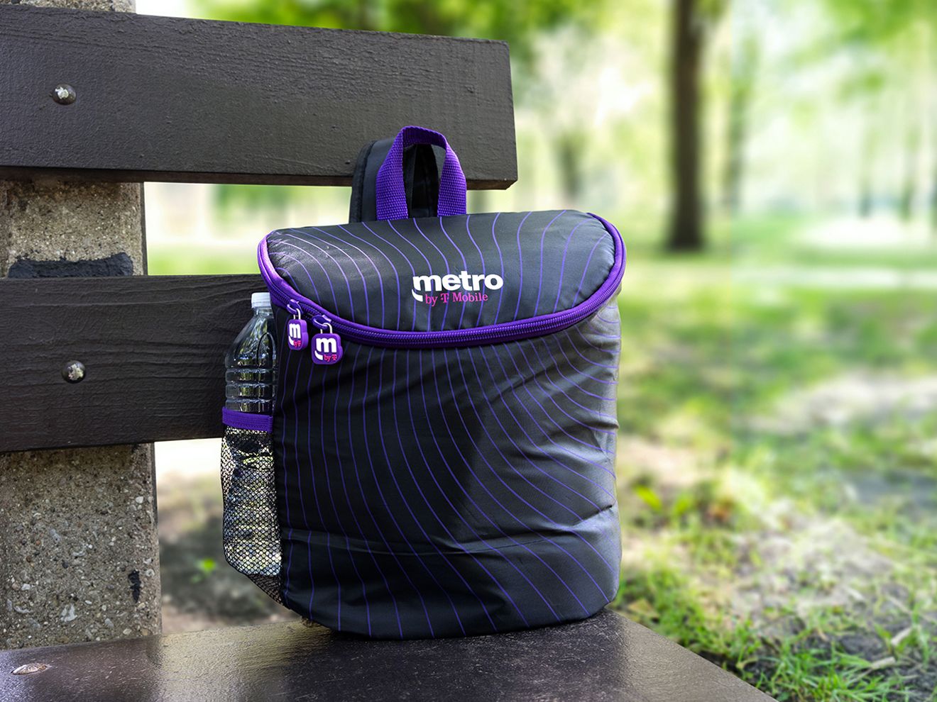 Purple, soft-sided Metro backpack cooler with side pocket for a water bottle sets on park bench.