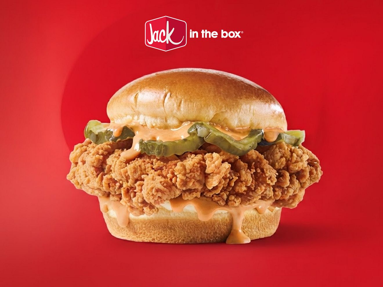 Un sándwich Cluck Chicken de Jack in the Box sobre un fondo rojo, con el logotipo de Jack in the Box flotando encima.