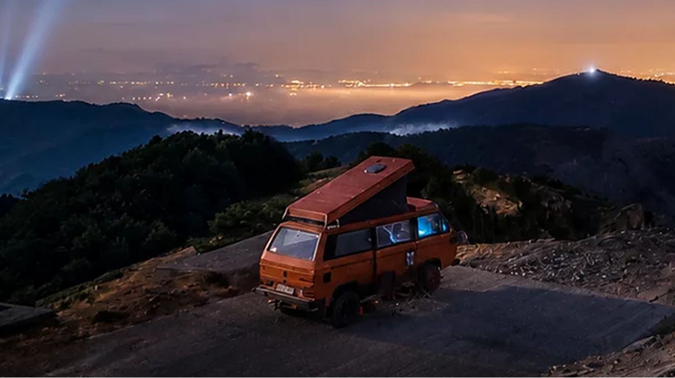 Camper van parked on a mountain cliff at sunset.