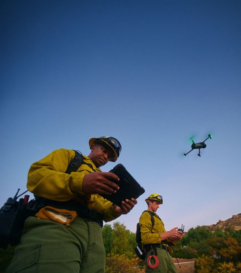 With a tablet, a worker controls a drone overhead.