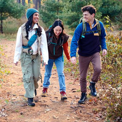 Two women and a man smile as they walk together through a forest with their JBL Clip five.