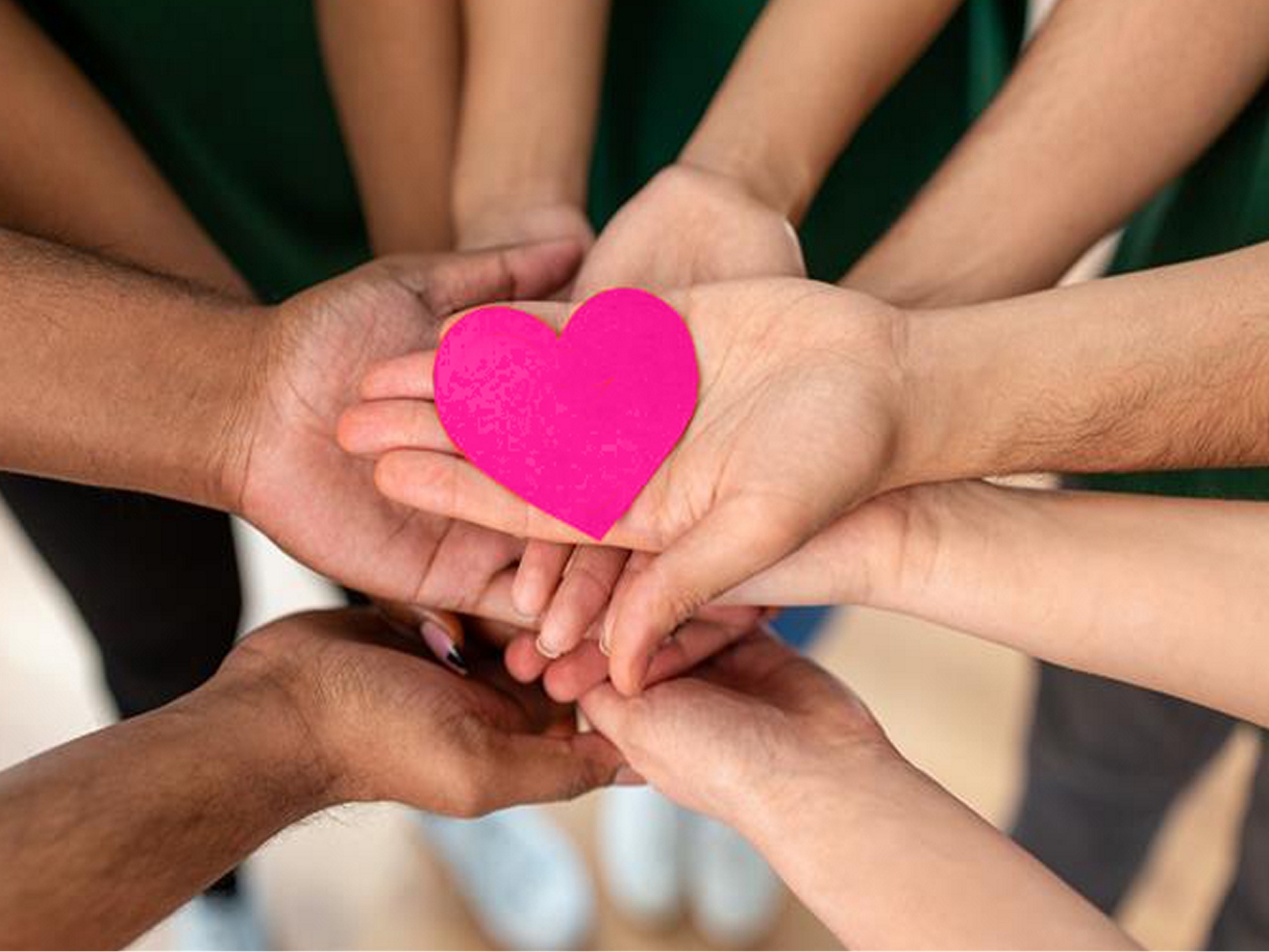 A group of hands holding up a pink, heart-shaped paper cutout.