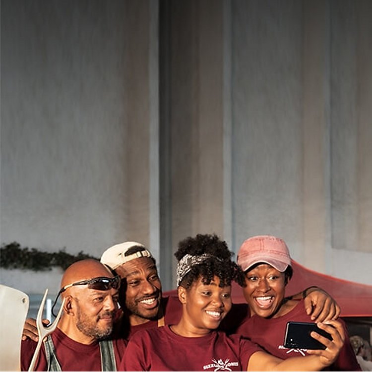 Four people standing close together and looking at a phone