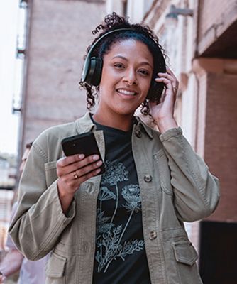 A woman walks in the city listening to her headphones through her smartphone.