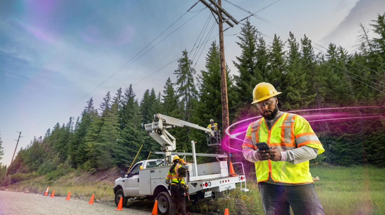 Utility worker wearing safety gear uses a tablet outdoors on a sunny day.