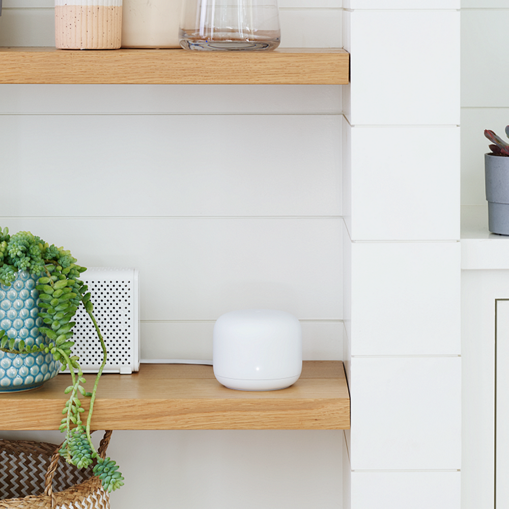 A Google Nest router on a shelf next to a plant and decorative vase.