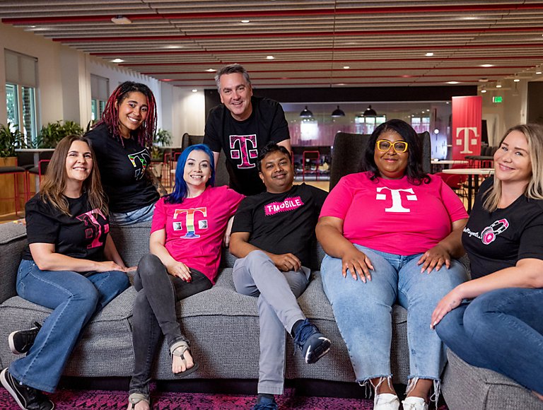 A group of diverse T-Mobile employees smile while sitting on a couch.