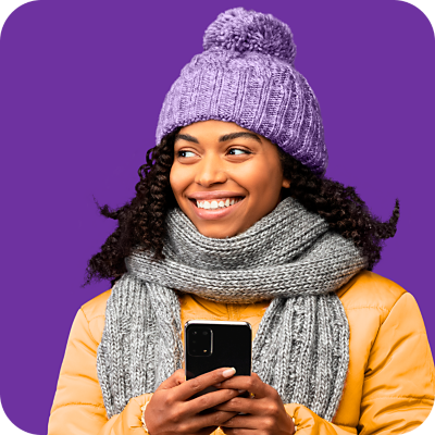 Woman wearing winter clothing smiling while she holds her phone.