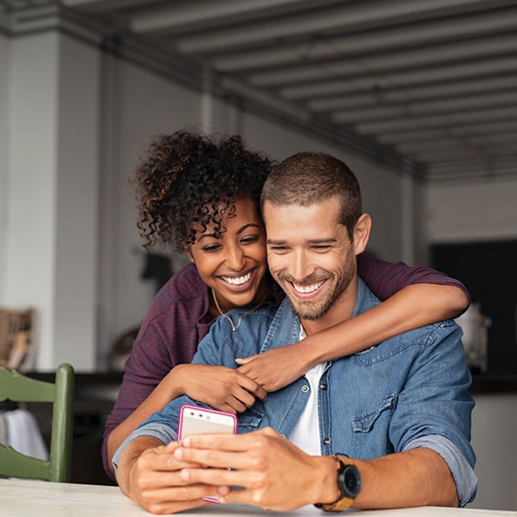 A man and a woman smiling while looking at a cell phone.