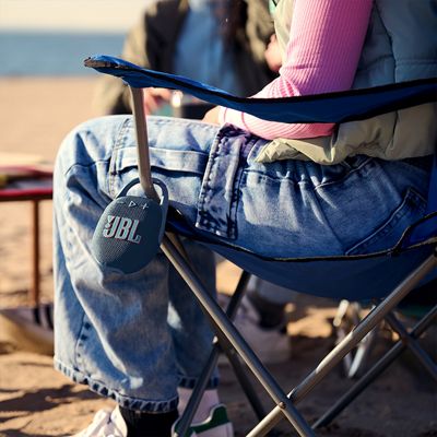 A JBL Clip five hangs on a woman’s chair at the beach.