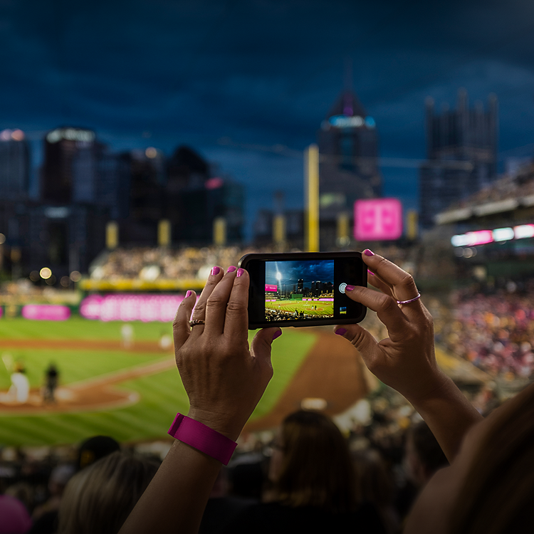 At a baseball park, two hands hold up a phone recording a Major League baseball game.