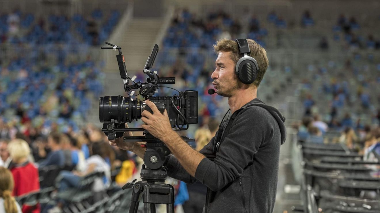 A person operates a professional-grade camera from the floor of an arena. 