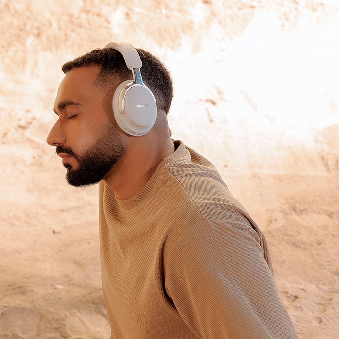Man closes his eyes contemplatively while listening to music on silver headphones.