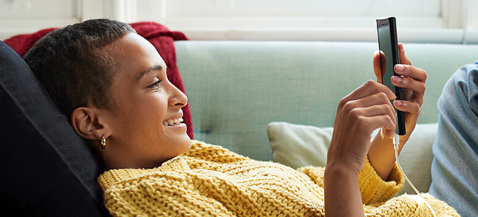 A woman lounging on a couch as she smiles at her phone