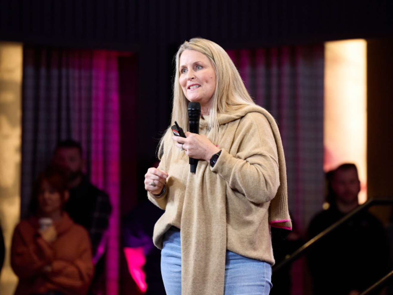 Deanne King smiles while she speaks to a crowd with a microphone.