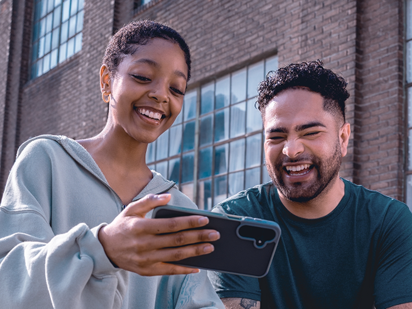 A woman and a man watch a video on a mobile phone.