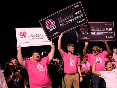 A group of students wearing magenta hold big checks in the air.