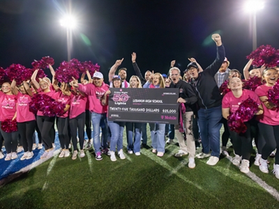 A group of students wearing magenta hold big checks in the air.