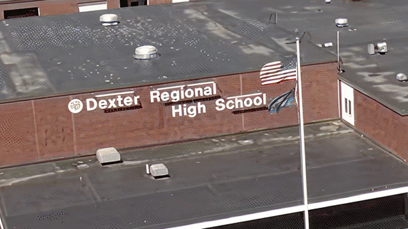 An aerial view of Dexter Regional High School, a brown building, with an American flag out front.