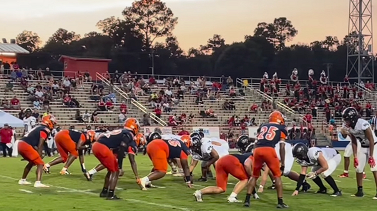The Escambia High School football team, in navy and orange uniforms, take the field