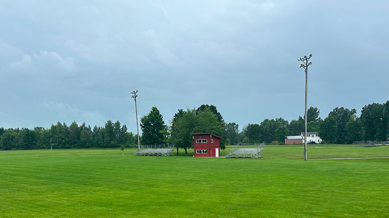 A vibrant green field with a small red building in the distance.