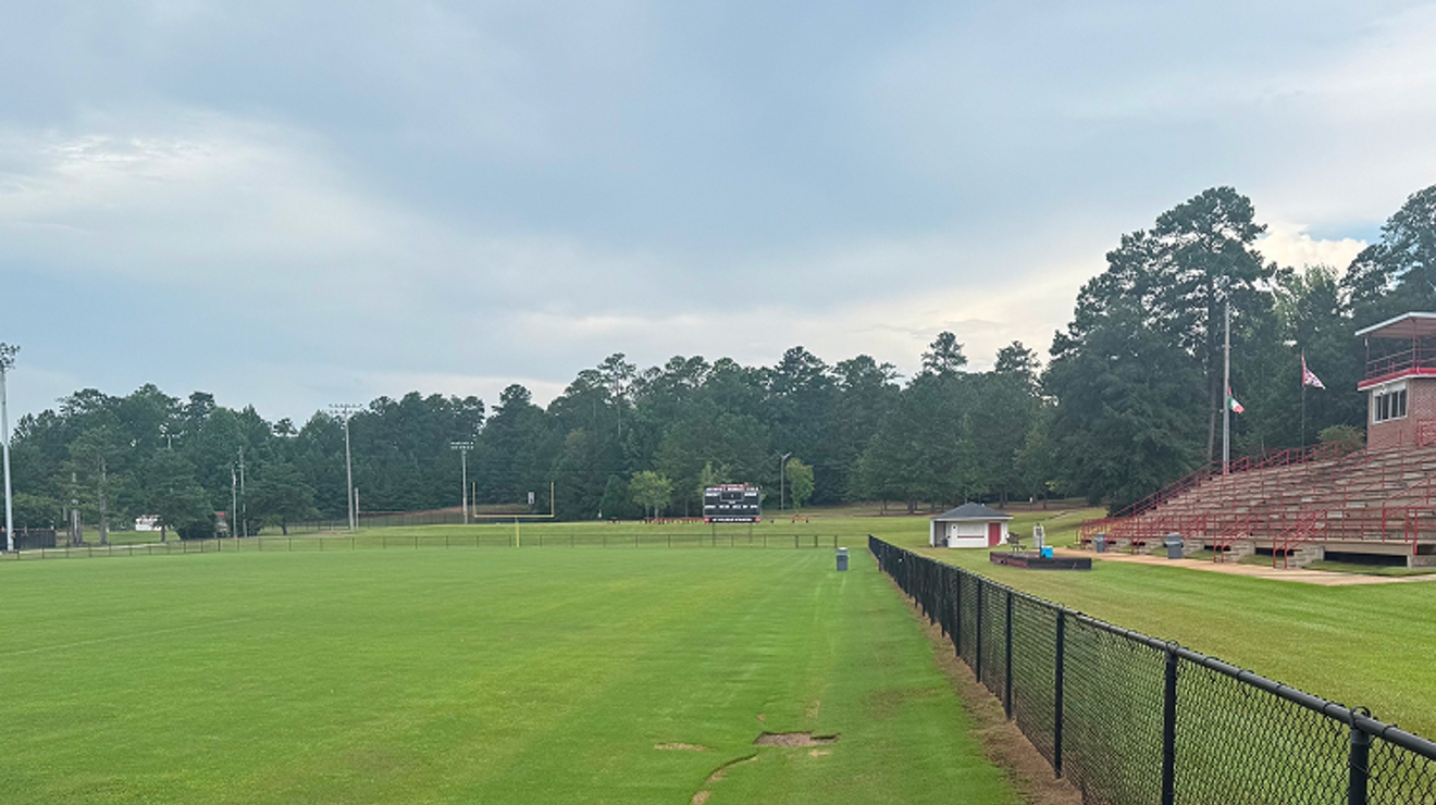 A vibrant green football field with stands in the distance.