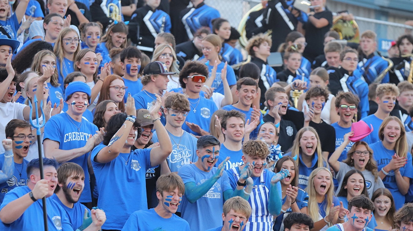 A blue and silver crowd of students cheer at a football game.
