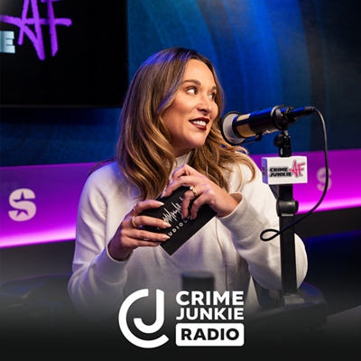 A woman in a podcast studio speaking into a microphone while holding a notecard and smiling. Crime Junkie Radio logo is at the bottom.