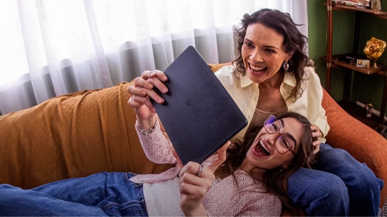 Mom and daughter laugh on couch while they watch a video on a Revvl Tab 2. 