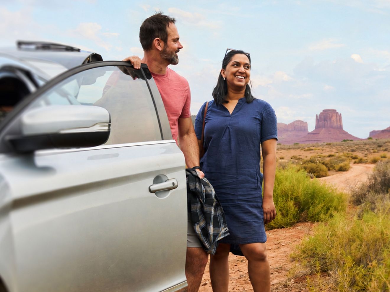A couple looks at scenery standing next to their car. 