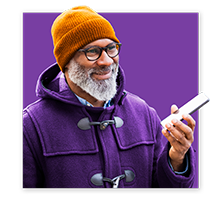 Man in a warm coat and a beanie smiles at his smartphone