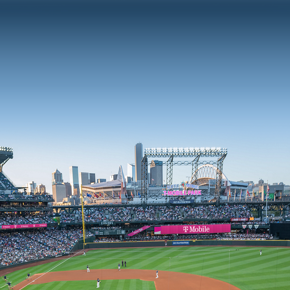 From the stands, T-Mobile Park with players on the field and the Seattle skyline in the distance