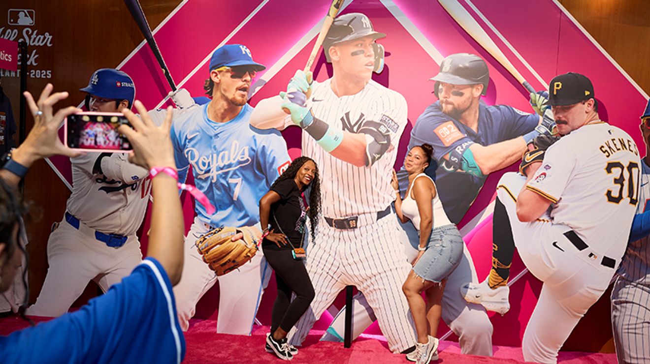 Two friends posing for a picture in front of a large collage of MLB players.
